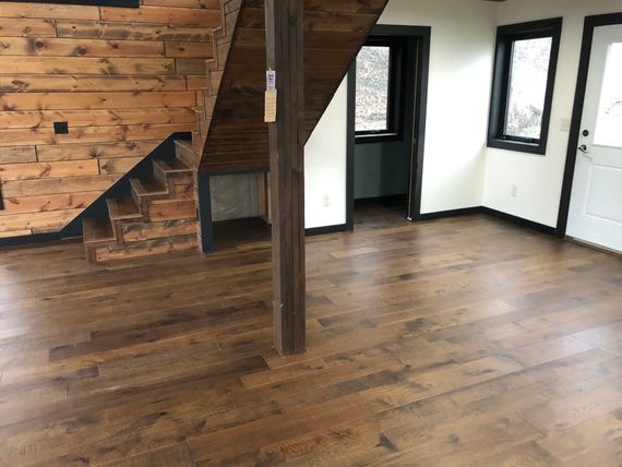 Empty room with wooden floor, exposed wood stairs, and large windows with white walls.