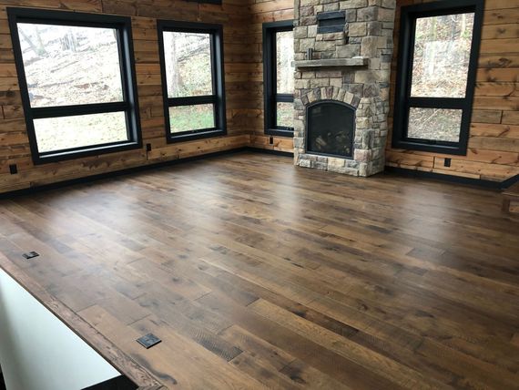 Empty rustic room with hardwood floors, brick walls, large windows, and a stone fireplace.