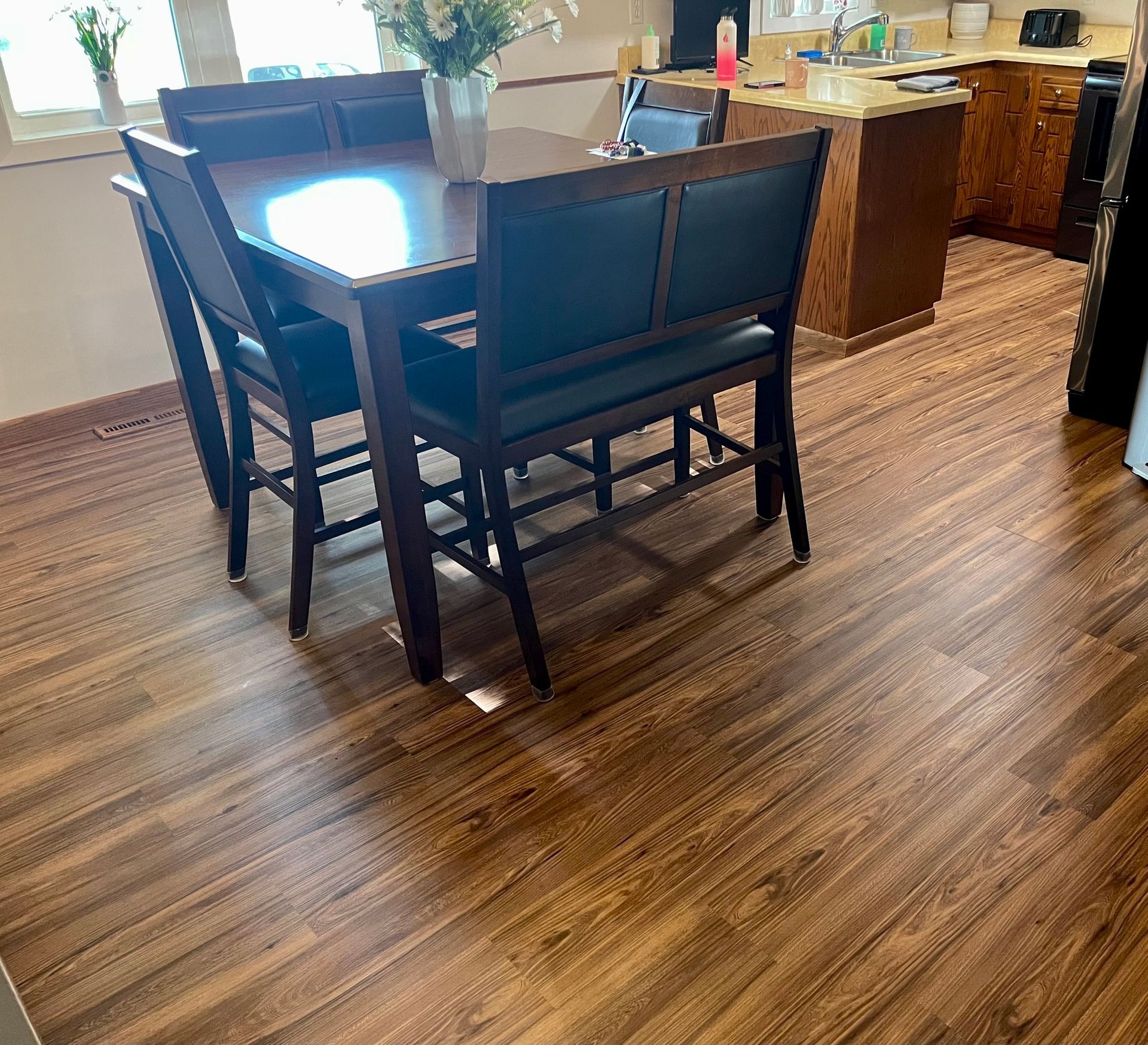 Dining area with dark wood table and chairs on a hardwood floor, near a bright kitchen counter.