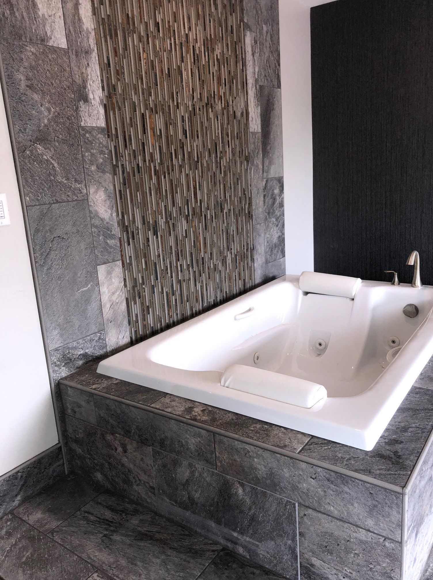 Modern bathroom with a white corner bathtub and dark stone wall tiles