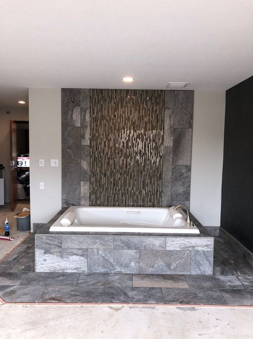 Modern bathroom with a freestanding tub, gray stone tile, and a textured mosaic accent wall.