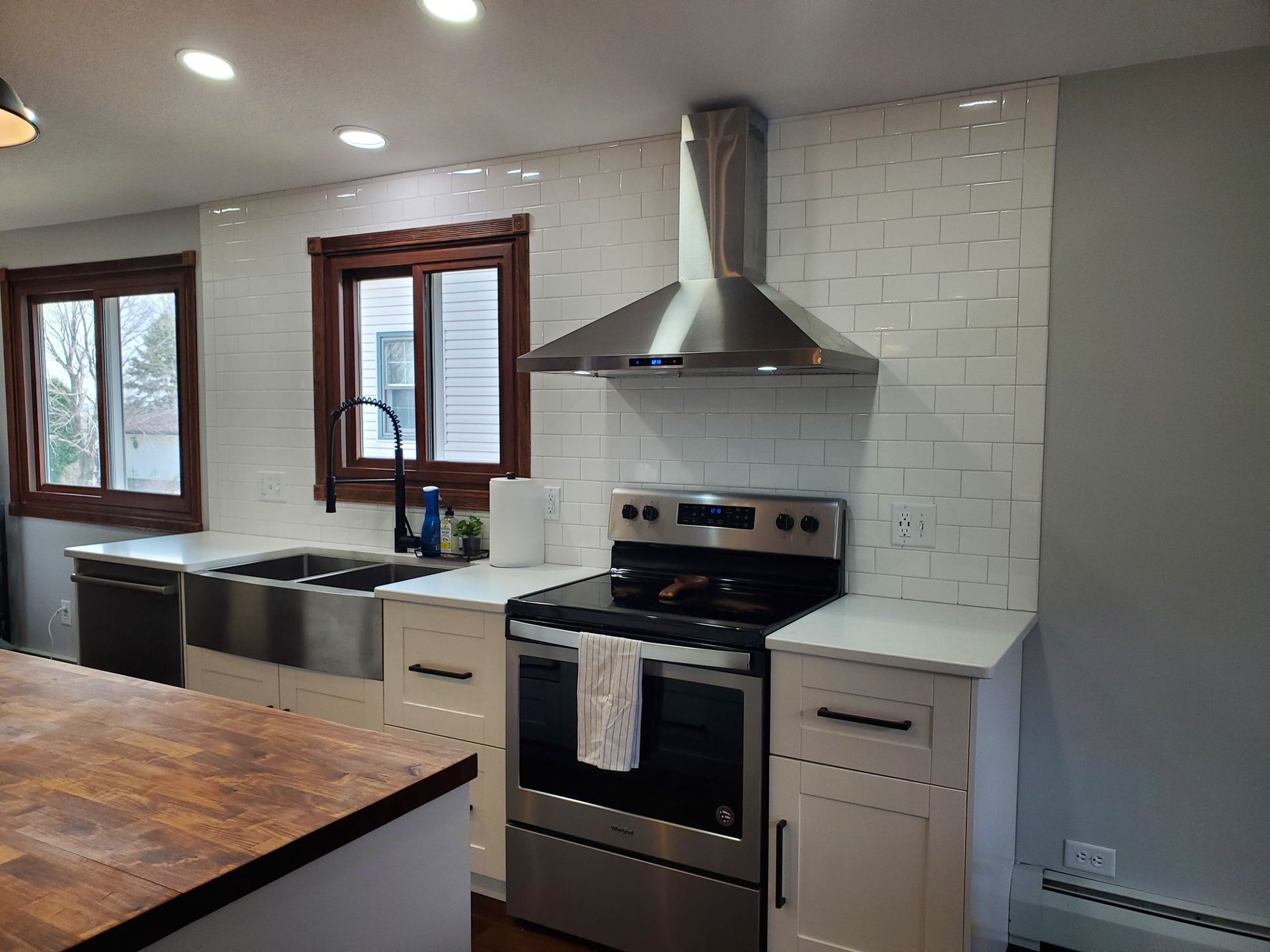 Modern kitchen with white cabinets, stainless appliances, wood island, and large windows