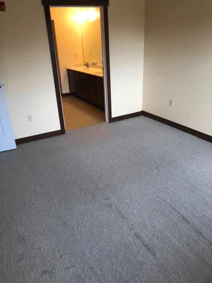Empty carpeted room with open doorway to a lit bathroom vanity area