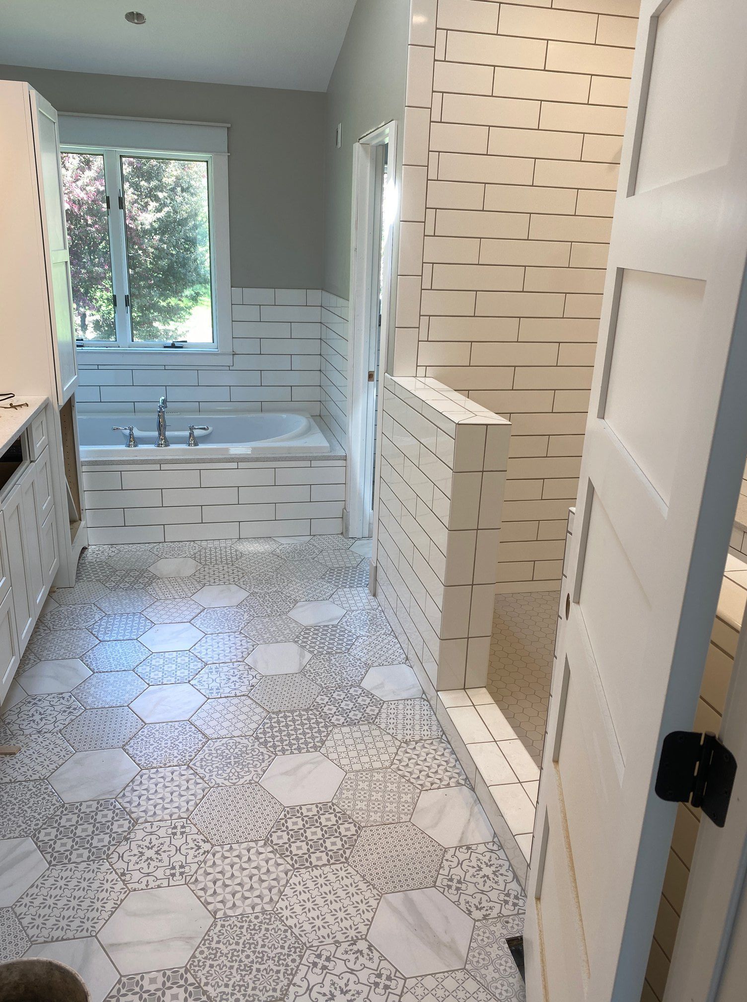 Narrow bathroom with patterned tile floor, white subway shower, vanity, and window at the end.