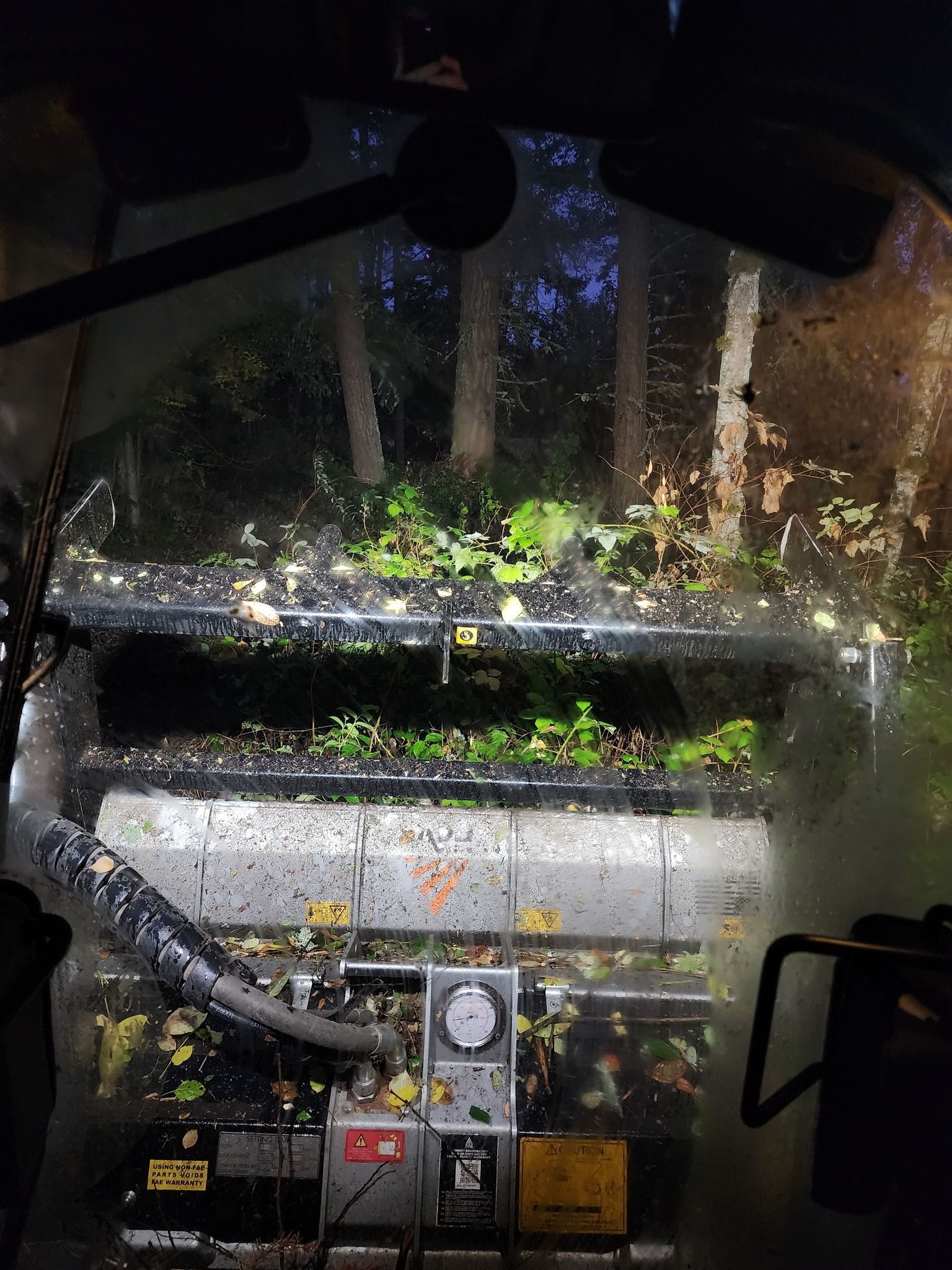 Rain-streaked window view of machinery and green plants in a dim industrial area
