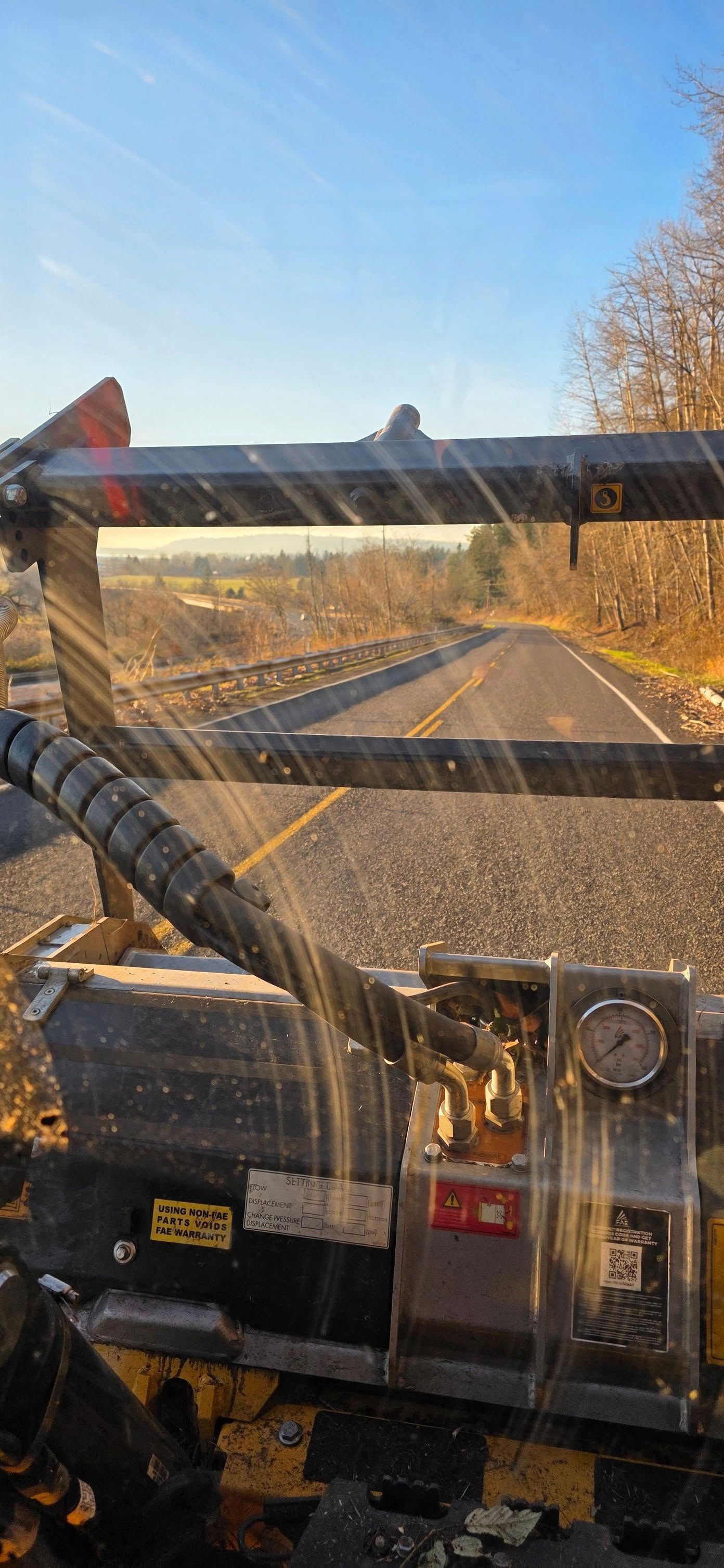 View from inside a vehicle driving on a sunny rural road with trees and fencing ahead