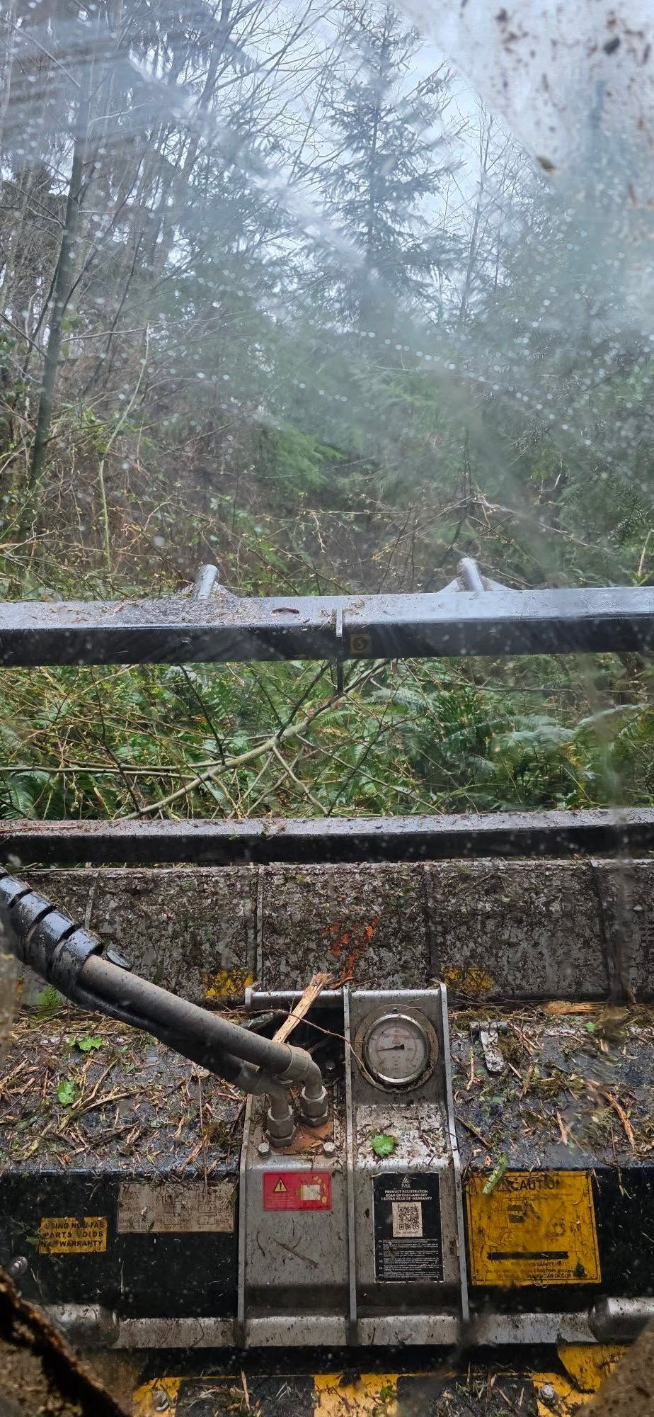 Rainy view through a truck windshield, with dashboard gauges and wiper blade visible against wet trees.
