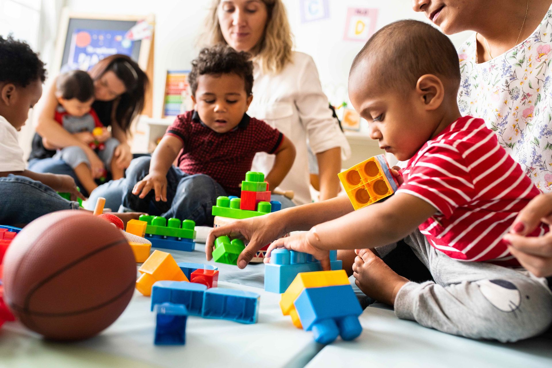 Infant toddler childcare center children building with bright plastic blocks on floor.
