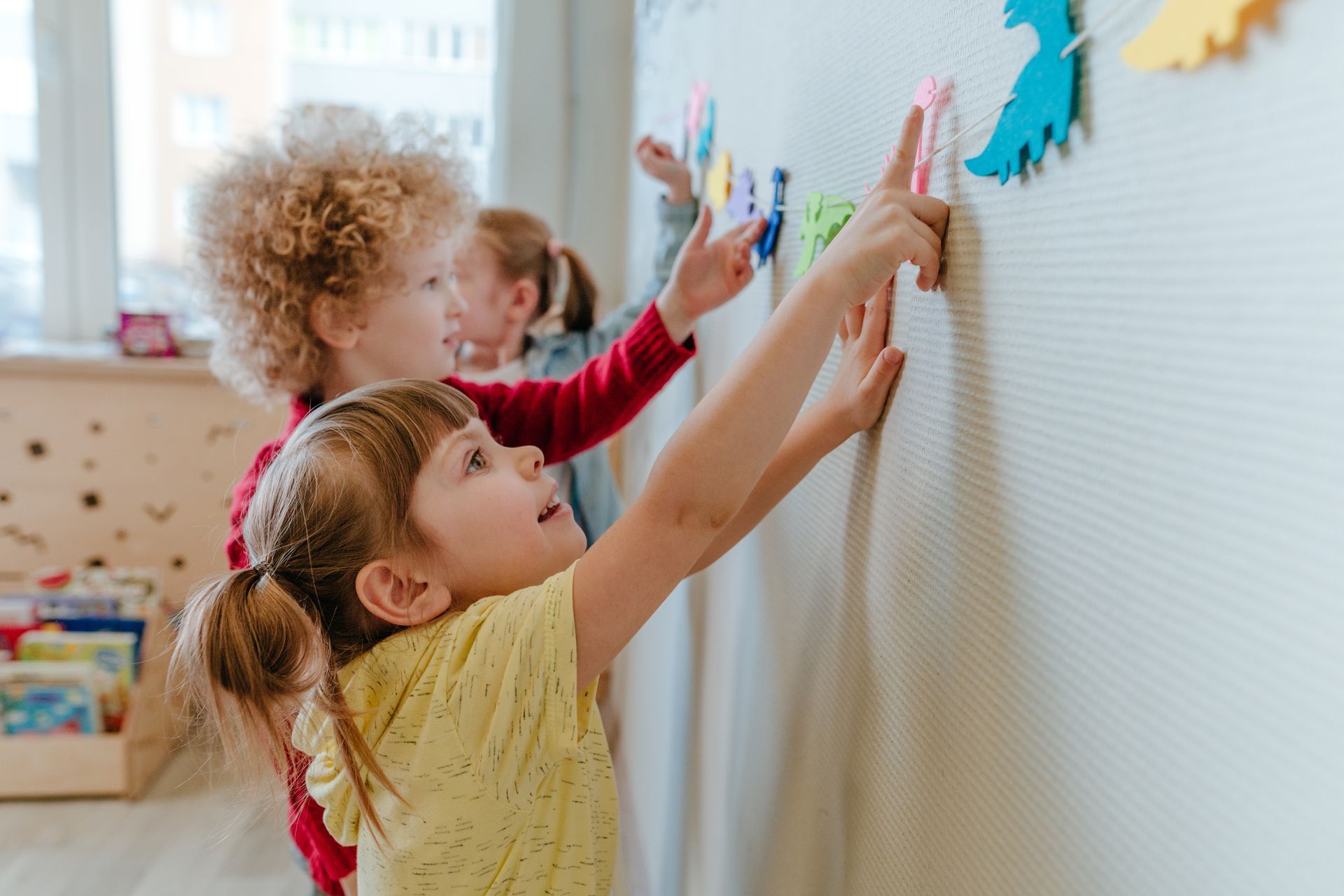 Children placing shapes on a classroom learning wall. Children placing shapes on a classroom learning wall.
