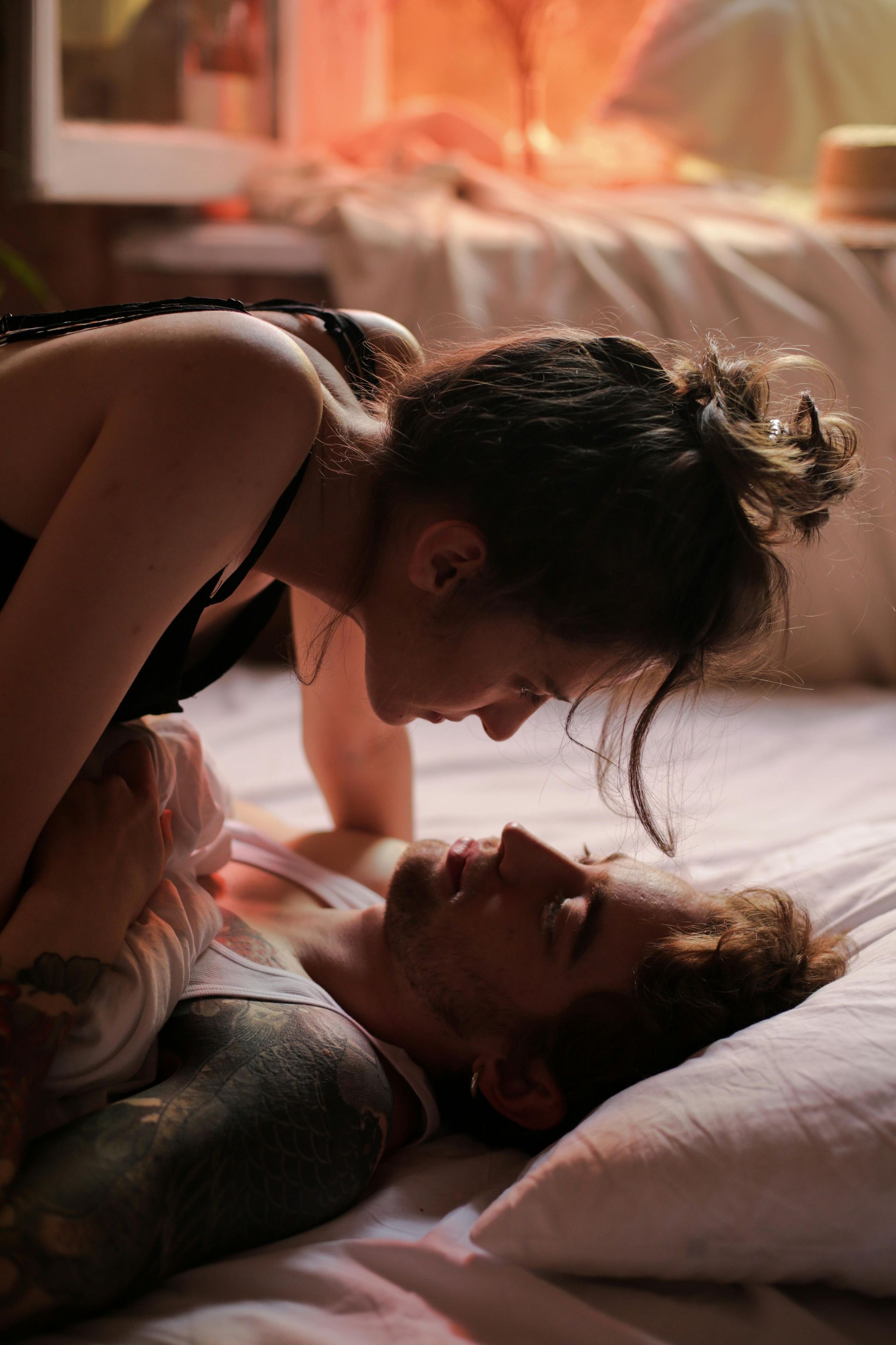 Two people lying on a bed, gazing closely at each other in warm, soft light.