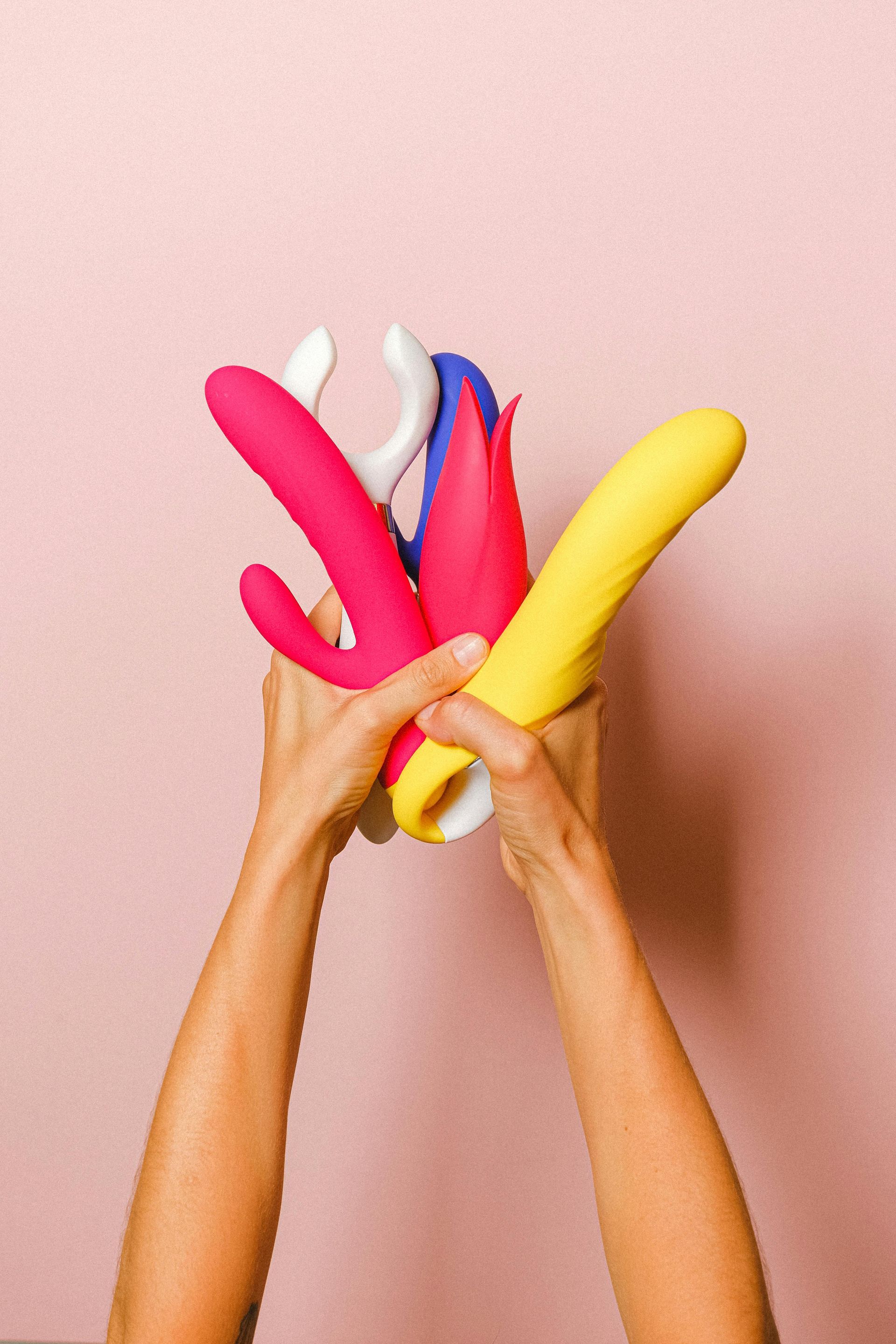 Hands holding colorful balloons or inflatable shapes against a pink background