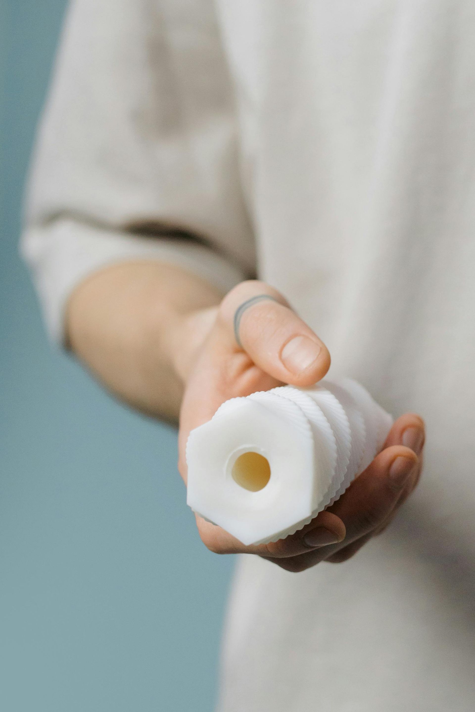 Hand holding a white ribbed medical tube with a beige opening against a gray background