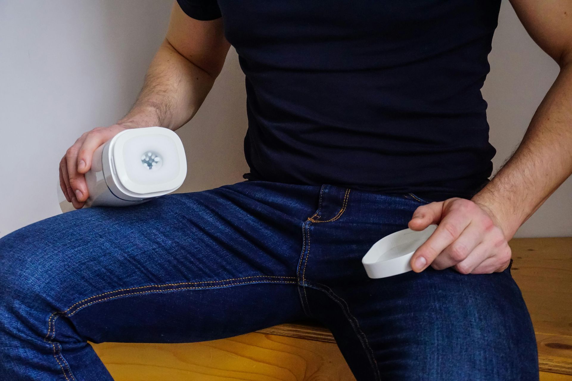 Person holding a masturbator device while seated in jeans and a black shirt