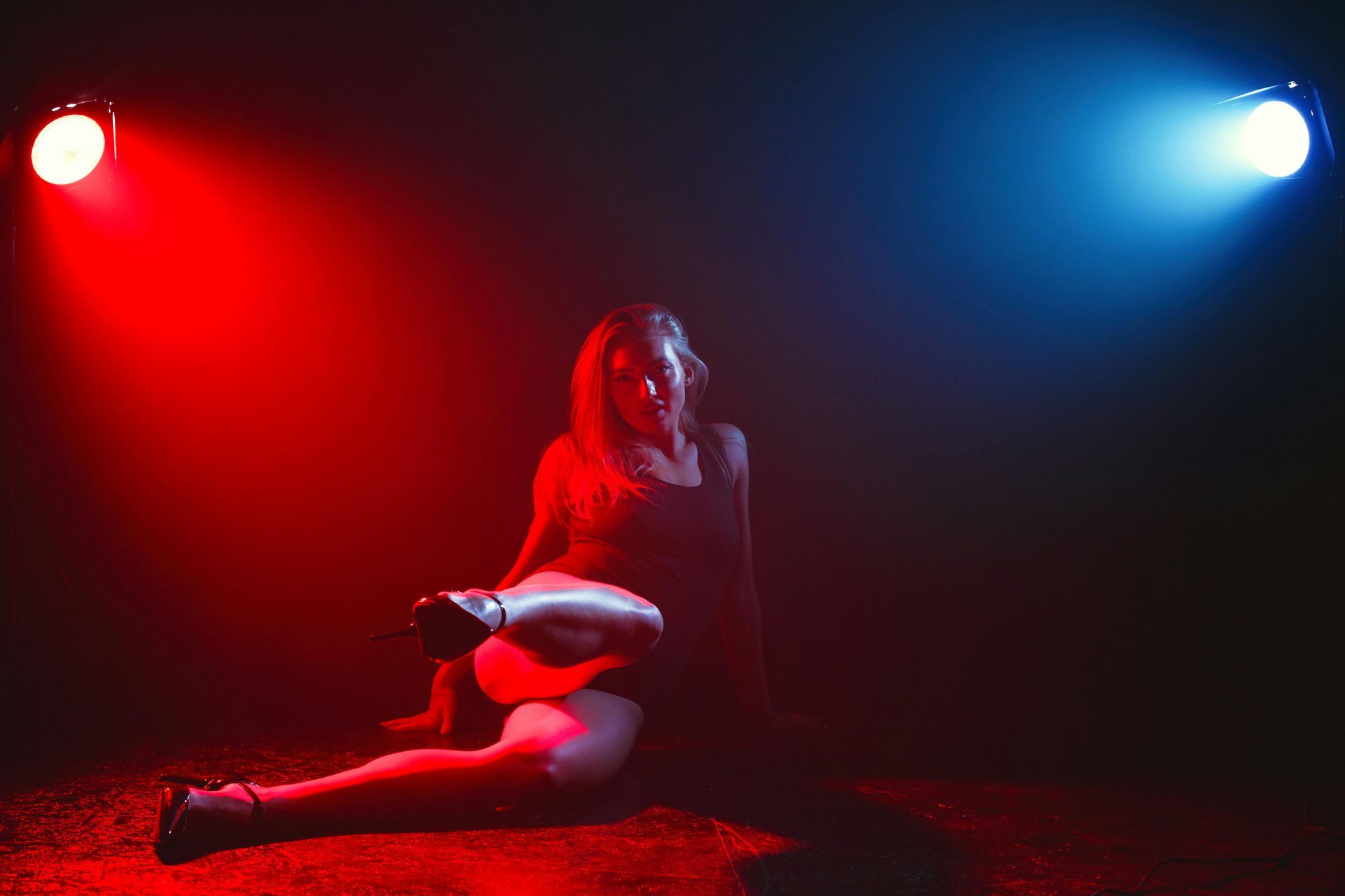 Person sitting on a red floor under dramatic red and blue stage lights, holding a white object