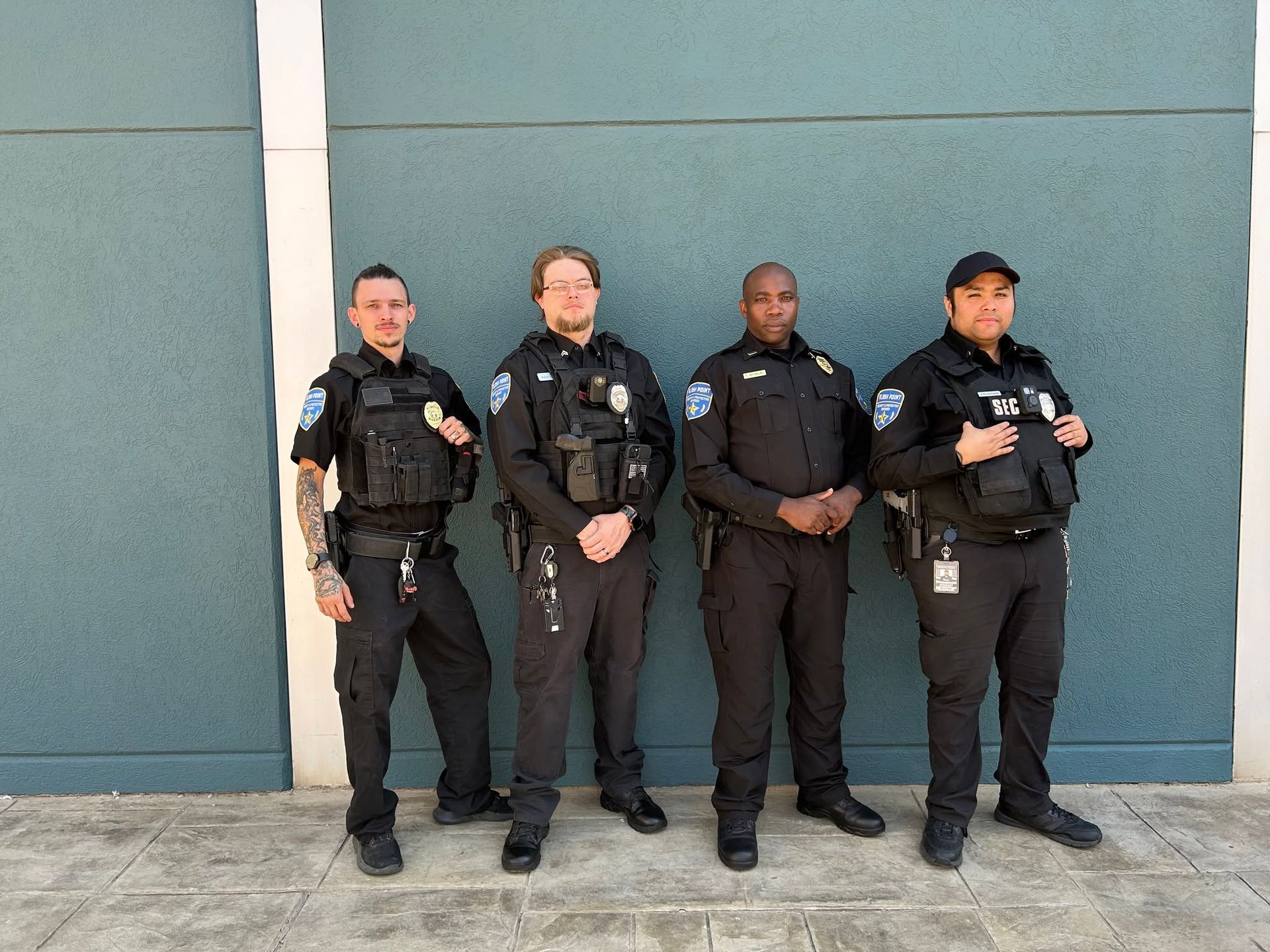 Four police officers standing in uniform against a blue wall outside.