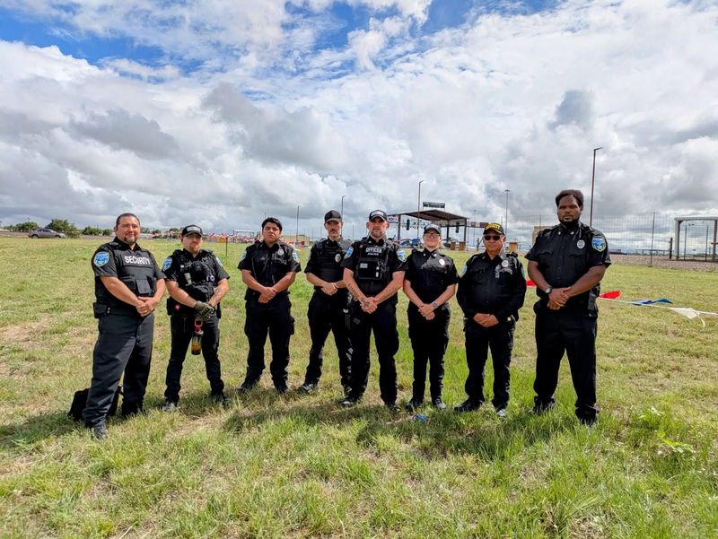 Seven uniformed officers standing in a grassy field under a cloudy sky