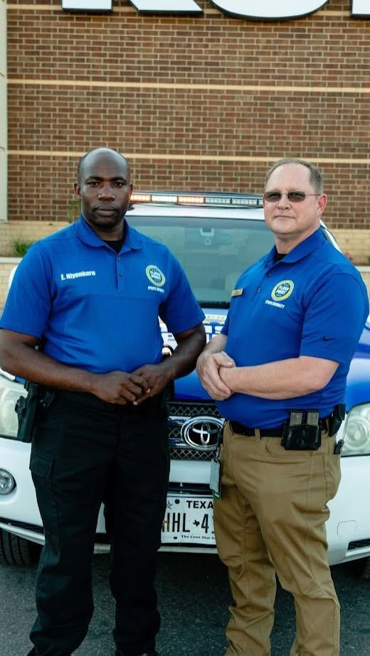 Two uniformed security guards standing in front of a brick building and a parked car.