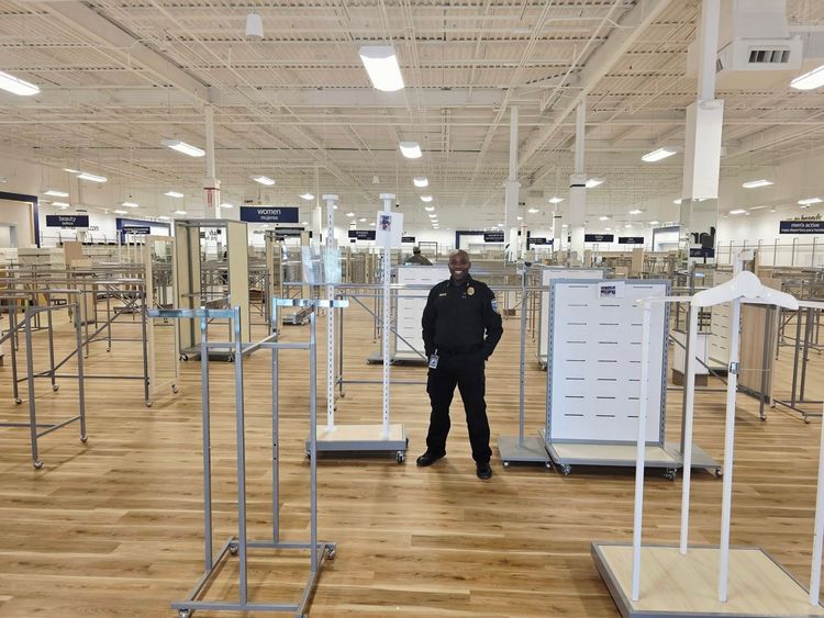 Empty retail store interior with clothing racks and a person standing in the center aisle