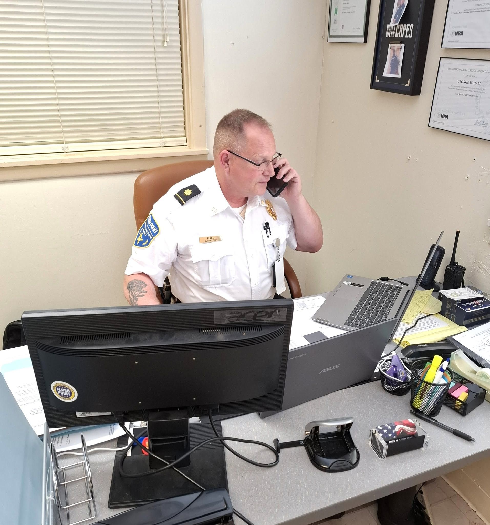 Person in a white uniform seated at a desk, talking on the phone in an office.