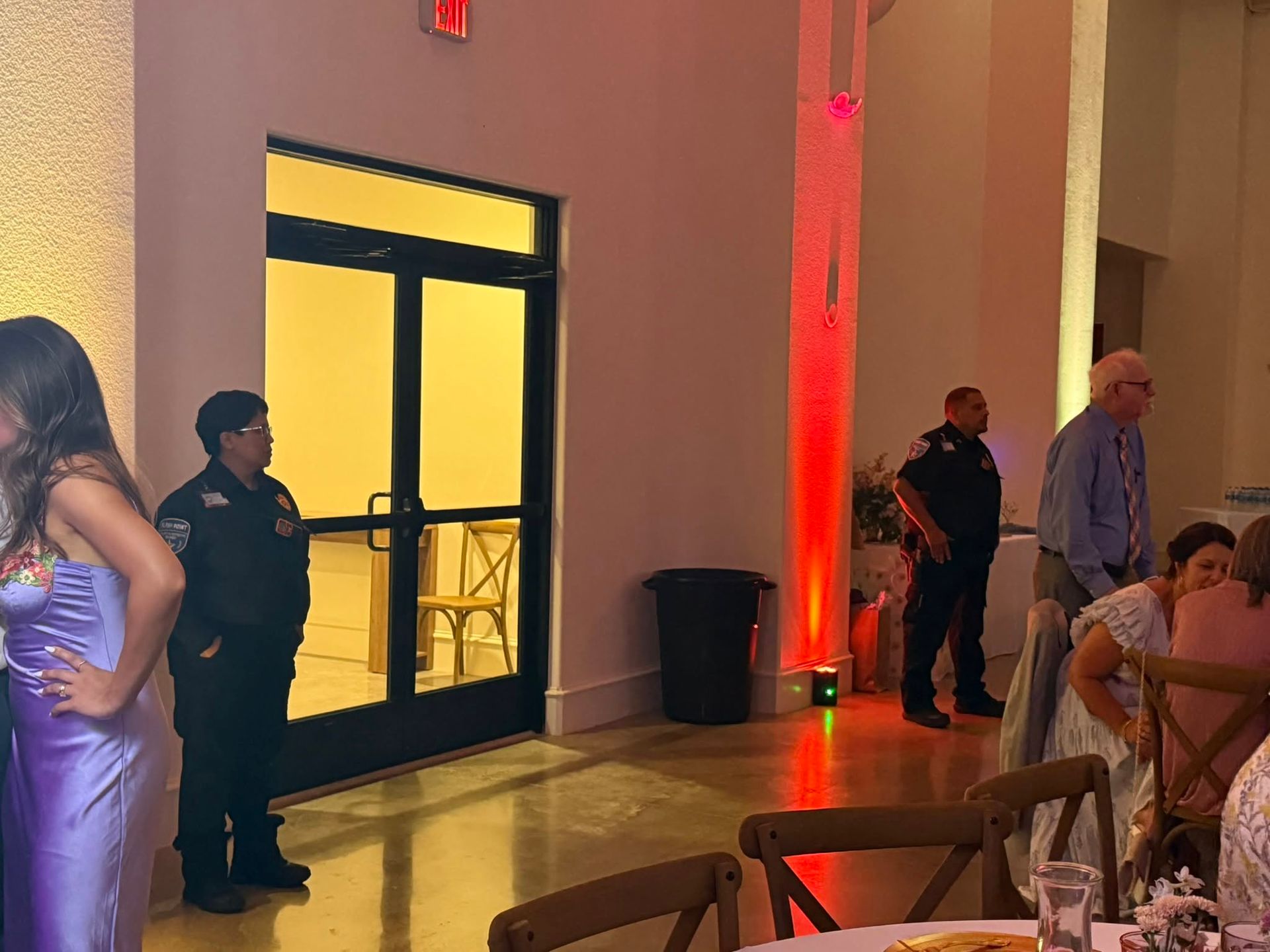 Dimly lit event hall with guests, a yellow-lit doorway, and red uplighting on the wall.