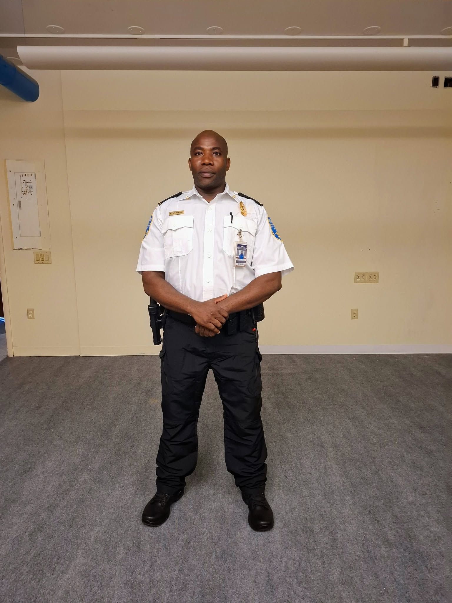 Person in a white uniform standing in a carpeted room with hands clasped in front.