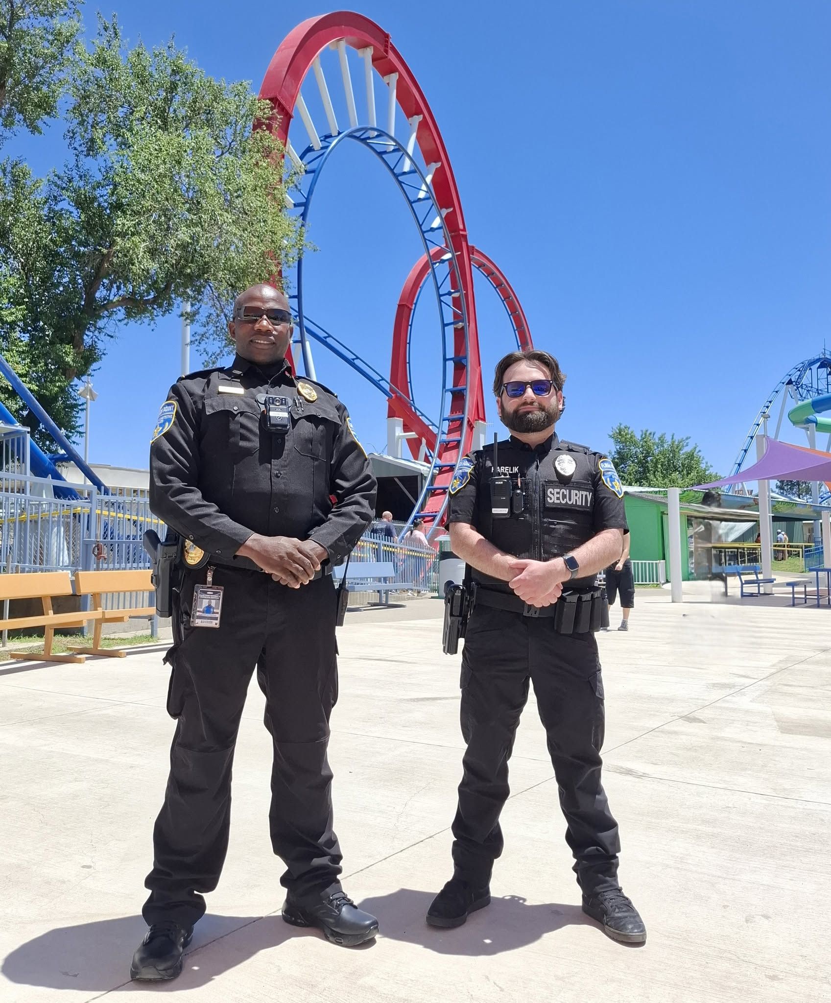 Two security officers standing in front of a red roller coaster on a sunny day.