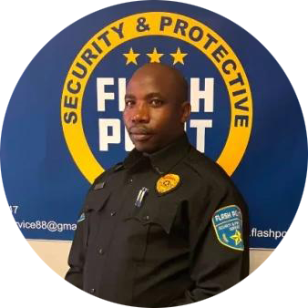 Security guard in black uniform standing before a blue and yellow “Security & Protective” logo wall