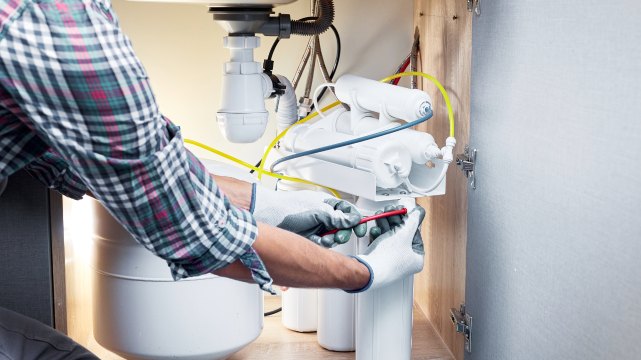 Plumber performing water filter service and leak detection under kitchen sink