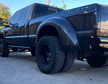 Black Ford F-350 Platinum dually truck with black rims and tinted windows parked on a city street.