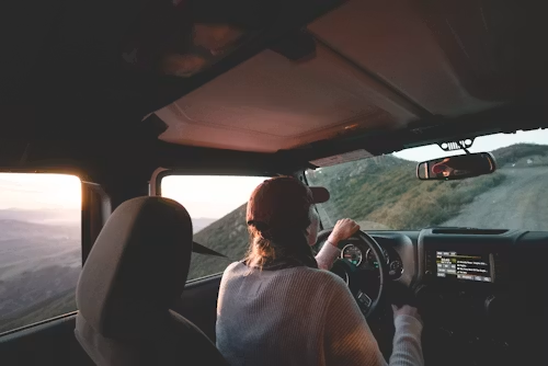 Driver steering a car on a mountain road at sunset, viewed from the back seat