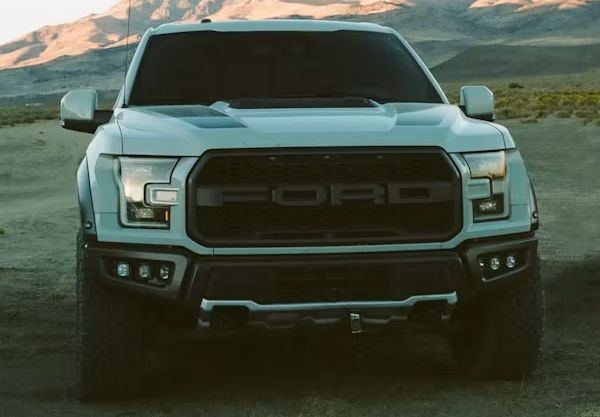 Front view of a black Ford pickup truck on a dirt road with mountains in the background