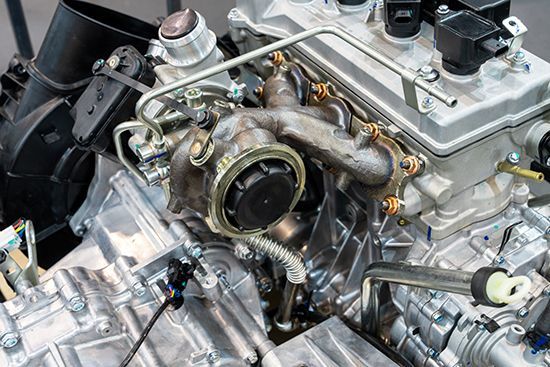Close-up of a car engine with a turbocharger, various pipes, and components in a workshop setting.