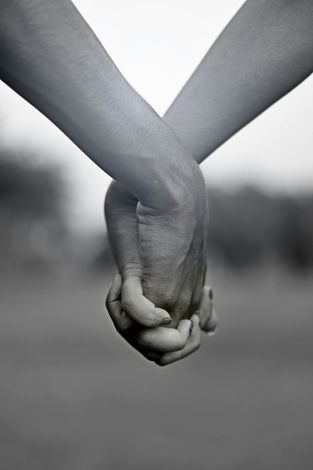 Two people holding hands, black and white, with blurred outdoor background