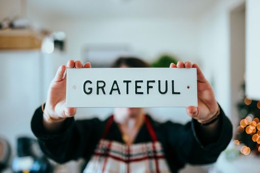 Person holding a sign that says “GRATEFUL” in a bright, blurred indoor setting