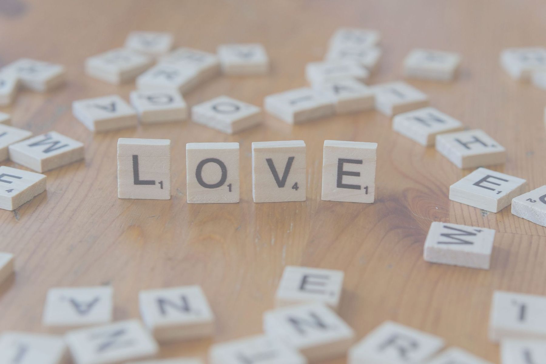 Wooden letter tiles spelling LOVE on a light tabletop with scattered tiles around them