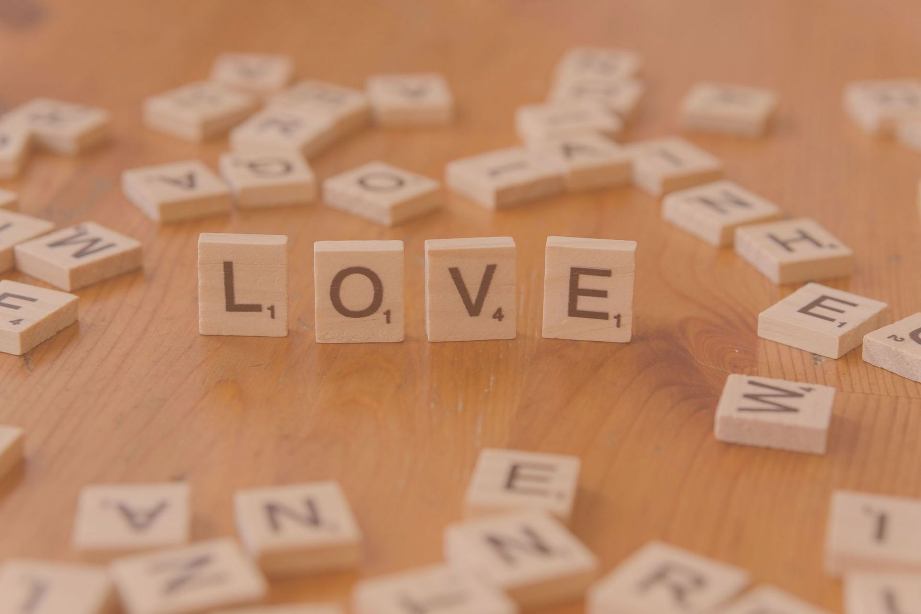 Scrabble tiles spelling LOVE on a wooden tabletop with scattered letter tiles nearby