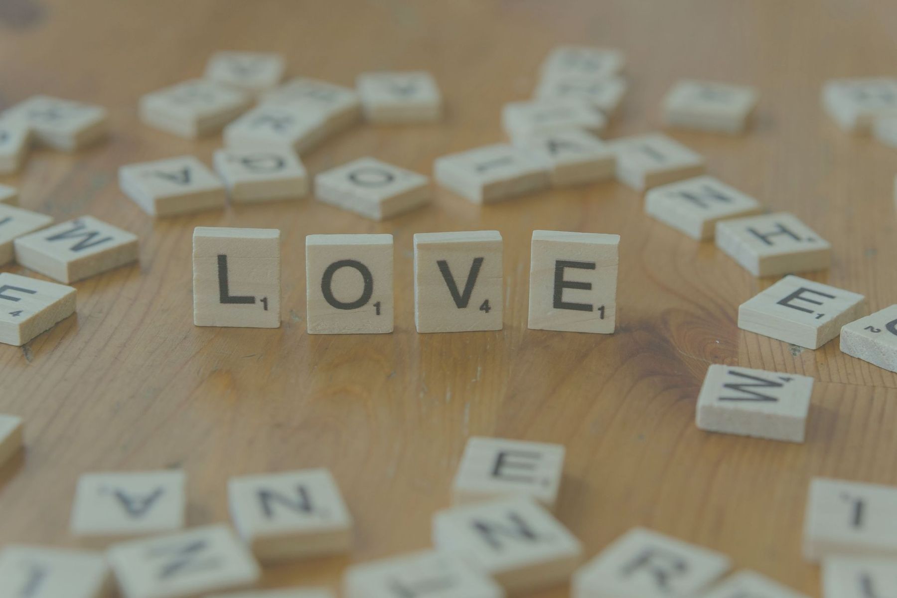 Wooden letter tiles spelling LOVE on a tabletop, with scattered tiles blurred in the background.