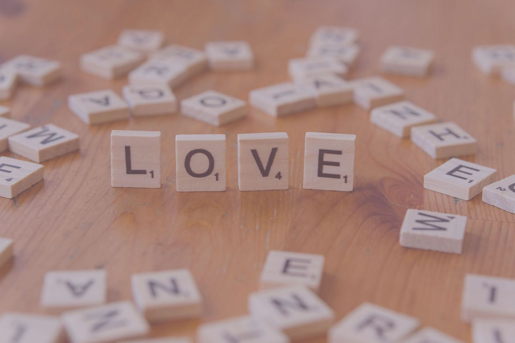 Wooden letter tiles spelling LOVE on a tabletop, with scattered alphabet tiles around them.