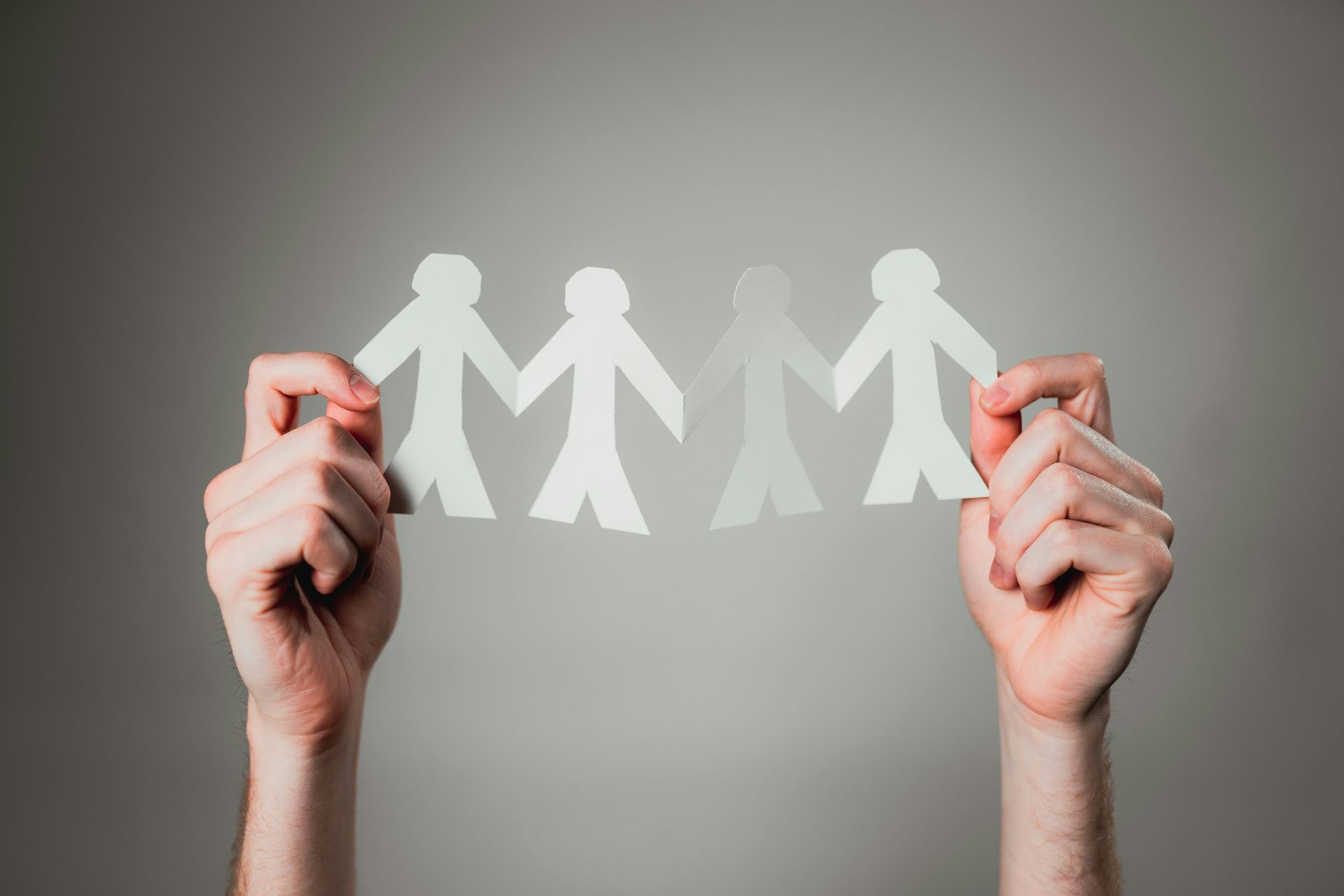 Hands holding a paper chain of connected people on a gray background