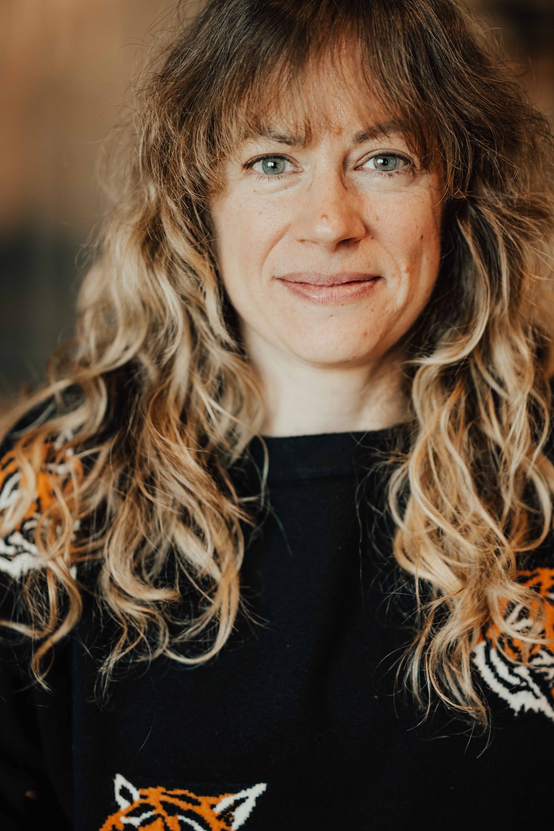 Woman with wavy blonde hair in a black sweater, facing the camera and smiling softly.