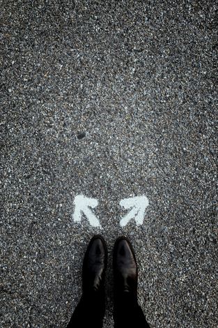Shoes standing on pavement between two white arrows pointing left and right