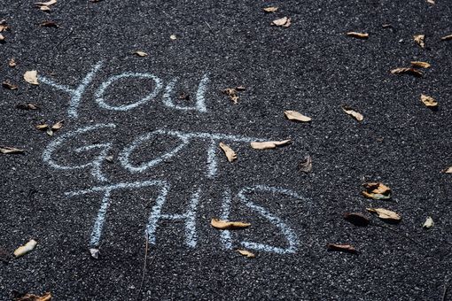 Chalk writing on dark pavement reads “YOU GOT THIS” with scattered leaves nearby.