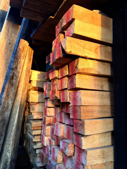Vigas de madera apiladas en un taller, con la cálida luz del sol iluminando sus extremos.