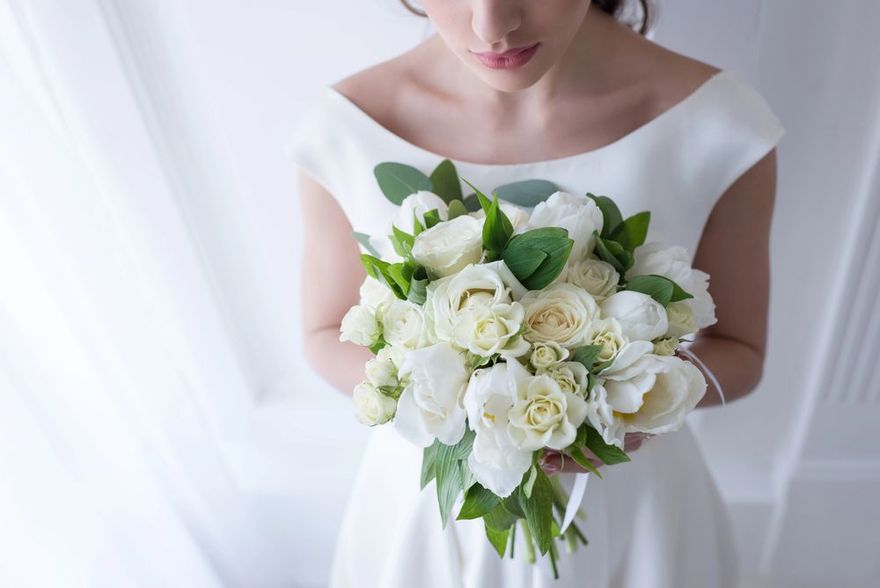 Sposa in abito bianco che tiene in mano un bouquet di fiori bianchi e verde.