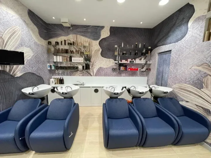 Salone moderno con poltrone lavatesta blu, lavandini bianchi e una parete decorativa con motivo grigio.