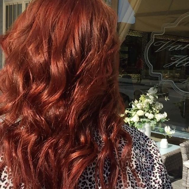 Lunghi capelli ramati ondulati visti da dietro, con una composizione floreale sullo sfondo.