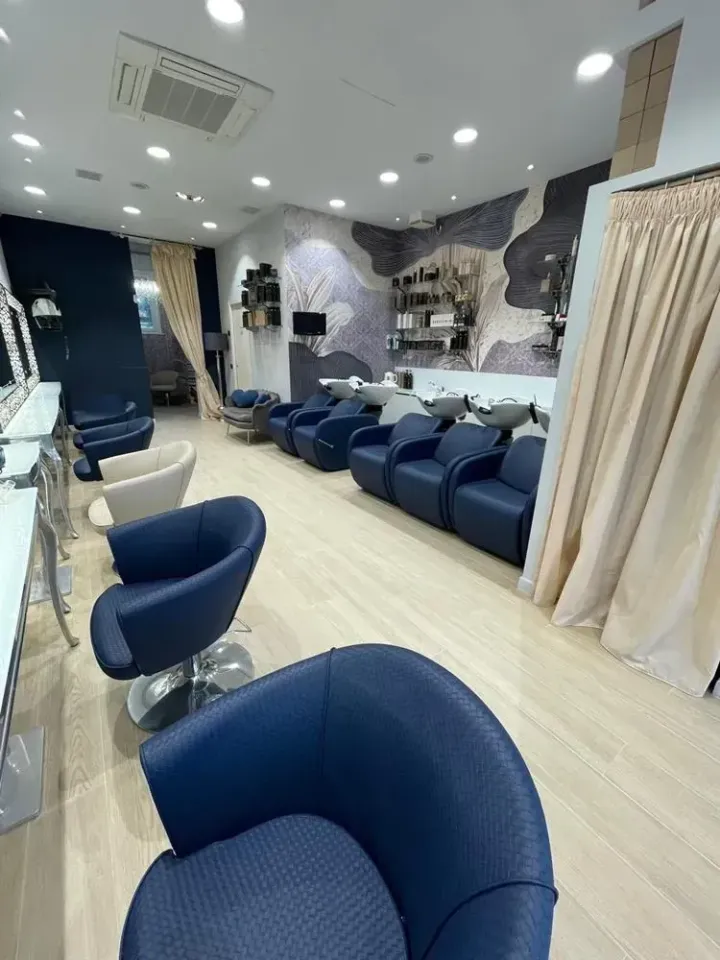 Sala d'attesa moderna della clinica con sedie blu, tende color crema e luci brillanti a soffitto.