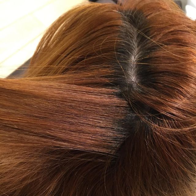 Primo piano di capelli castani con riga centrale ben visibile e radici scure.