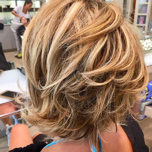 Primo piano di un taglio di capelli corto biondo scalato con riflessi caramello, seduto su una poltrona da parrucchiere.