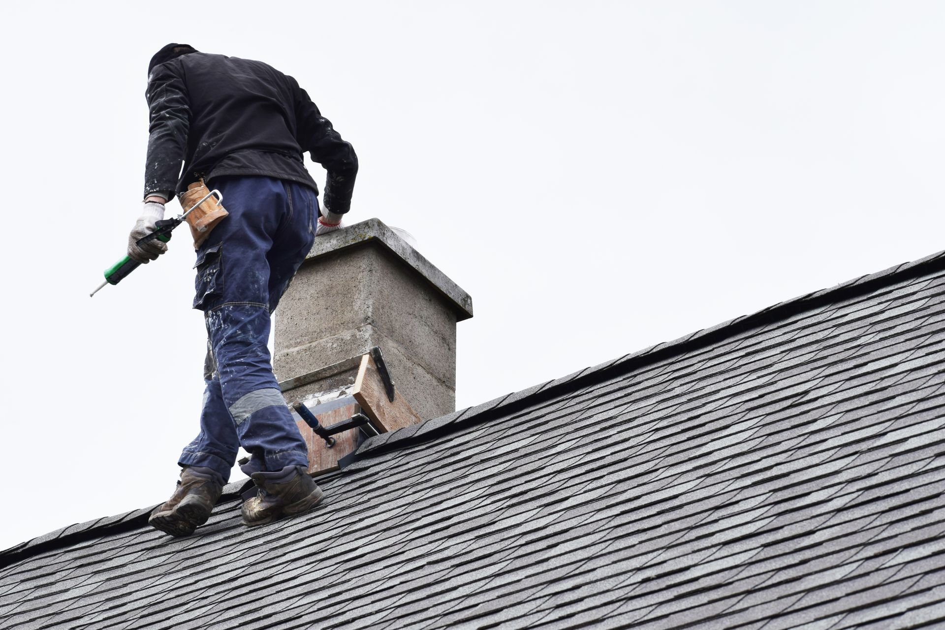 A worker fixing a chimney atop a grey slate roof of a residential house. A worker fixing a chimney atop a grey slate roof of a residential house.